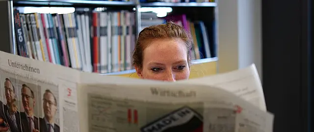 Frau, die den Wirtschaftsteil der Printausgabe einer Zeitung liest