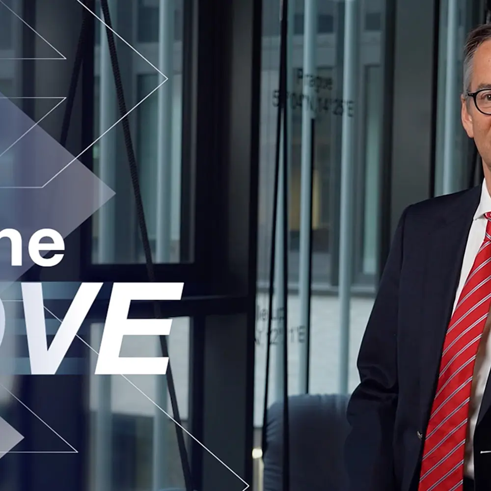 Geschäftsmann im Anzug steht in einem modernen Innenraum vor großem Schriftzug „Make the MOVE“ – Keyvisual für Testimonial-Video und vertrauensvolle Markenkommunikation im medizinischen Bereich.