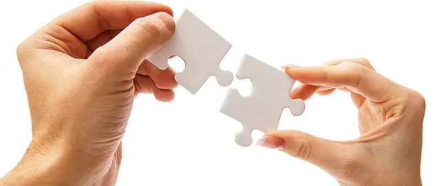 Zwei Hände halten jeweils ein Puzzleteil die zusammenpassen