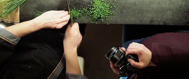 Foto auf dem zu sehen ist, wie ein Koch dabei fotografiert wird, wie er Schnittlauch schneidet
