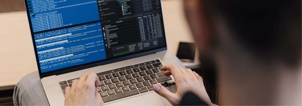 Person tippt auf einem Laptop mit geöffneten Code- und Terminalfenstern.