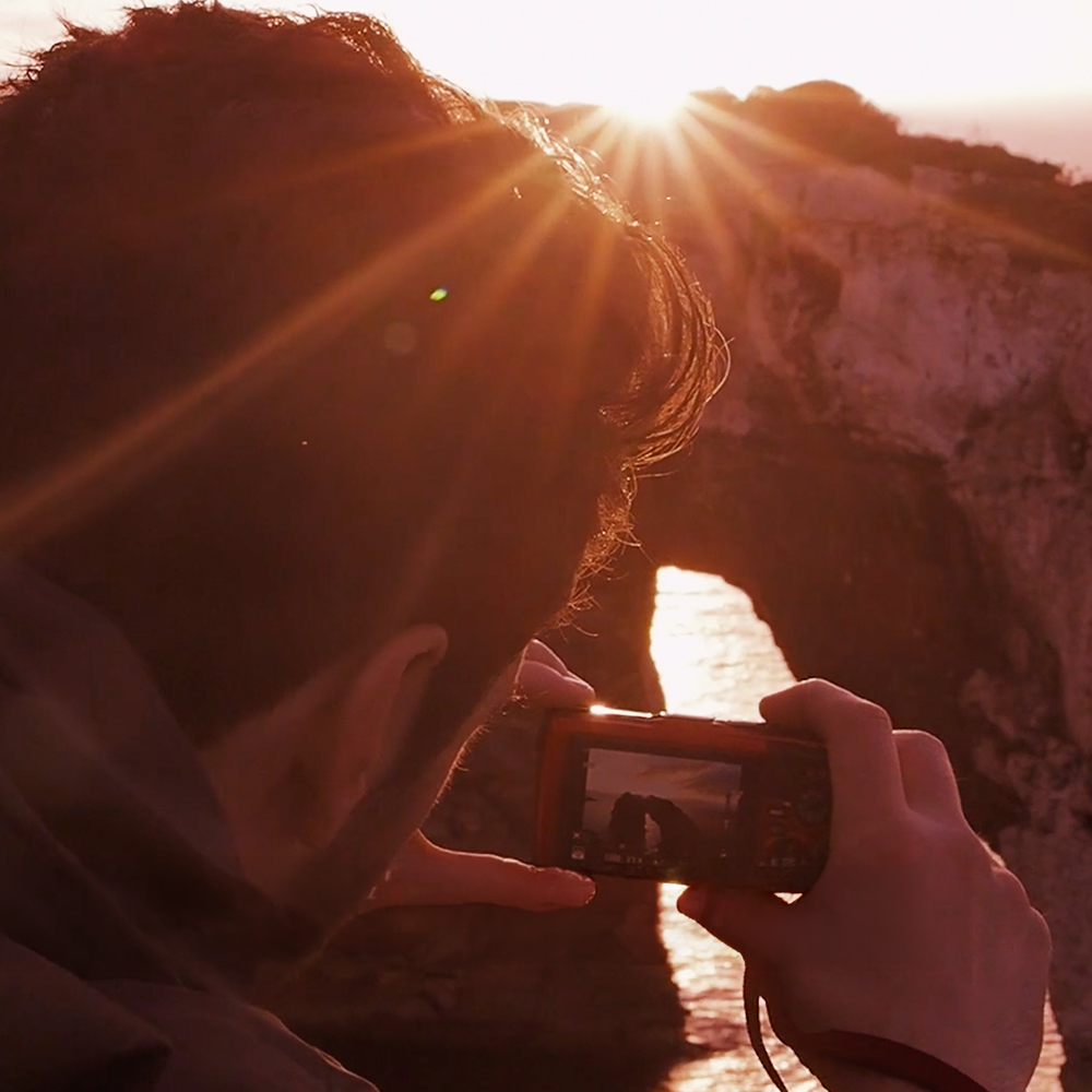 Mann fotografiert im Gegenlicht am Meer für Produktfilm